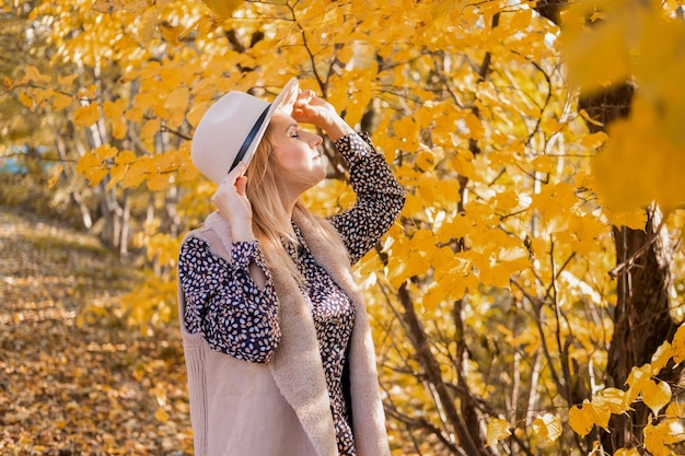 beautiful woman in fashionable clothes and hat drinks coffee in nature in fall