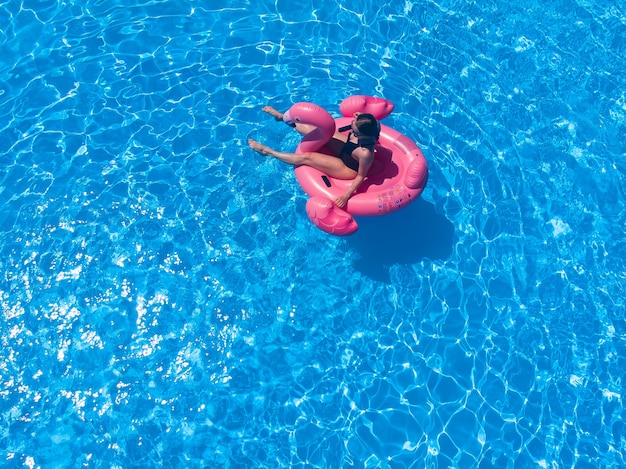 Beautiful woman on flamingo pool float in pool in the hotel, drone aerial view