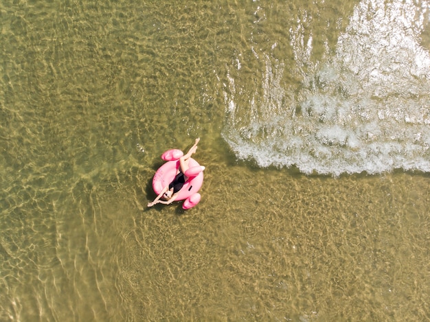 Beautiful woman on flamingo pool float in sea, drone aerial view