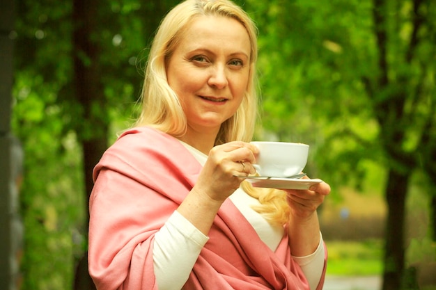 A beautiful woman forty years old dressed on a pink scar is drinking coffee in a cafe