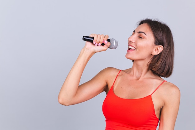 Beautiful woman on gray wall with microphone singing emotional favorite song happy positive cheerful