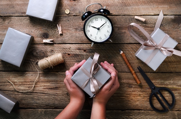 Beautiful woman hands holding gift box on wooden. Black alarm clock, pen, scissors