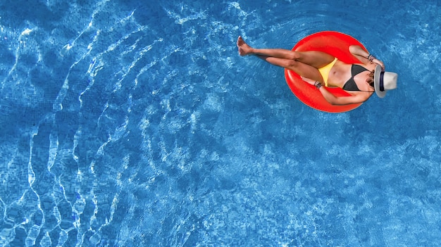 Beautiful woman in hat in swimming pool aerial view from above, young girl relaxes and has fun on inflatable ring