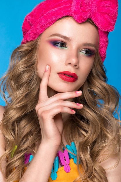 Beautiful woman in a hat with colorful makeup curls and pink manicure