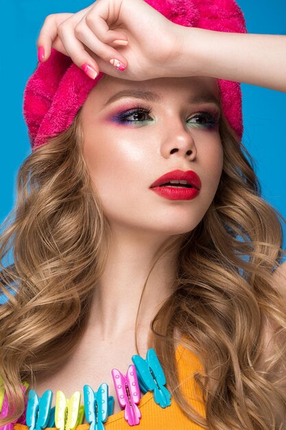 Beautiful woman in a hat with colorful makeup curls and pink manicure