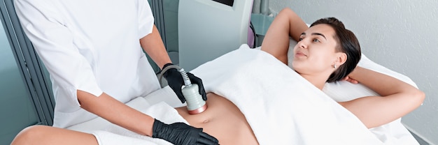 Beautiful woman having cavitation, procedure removing cellulite on legs and belly at beauty clinic