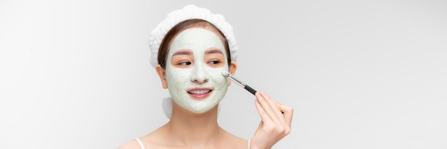 Beautiful woman having clay facial mask apply by beautician