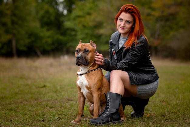 Beautiful woman and her American Staffordshire Terrier dog in fall park