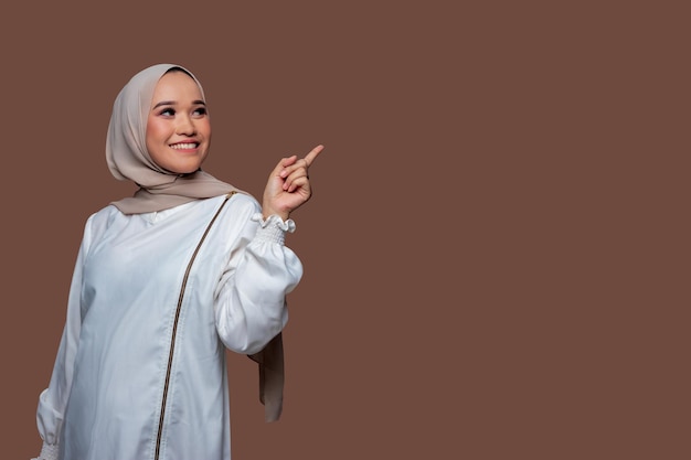 Beautiful woman in hijab is pointing to the right side with smile expression isolated on plain background