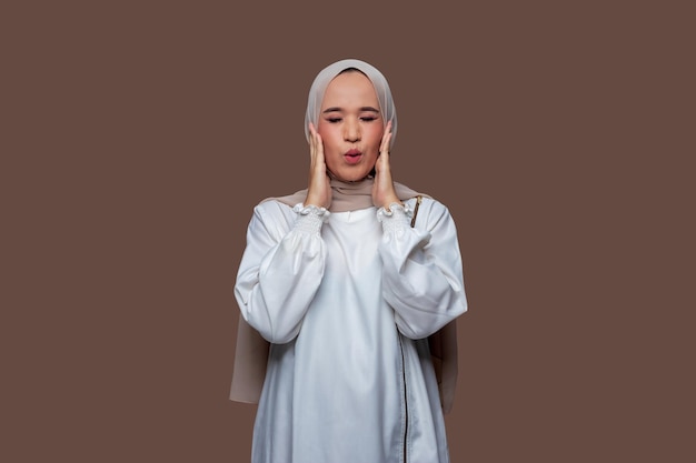 Beautiful woman in hijab was closed her eyes while holding her cheeks isolated on plain background