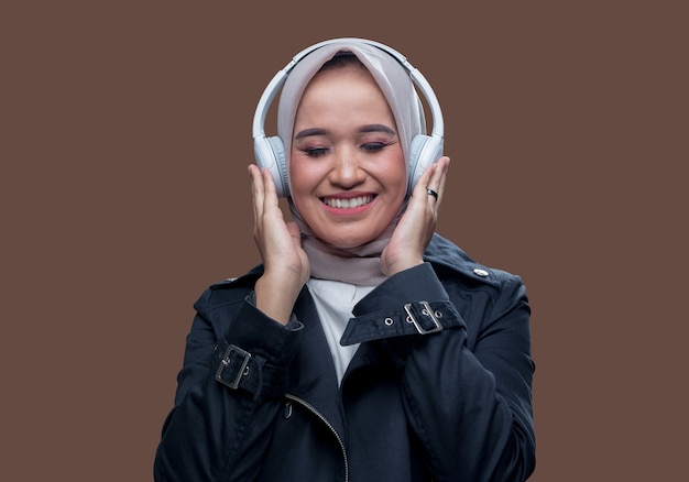 Beautiful woman in hijab was listening to music using wireless headphones with a smiling expression while closing her eyes