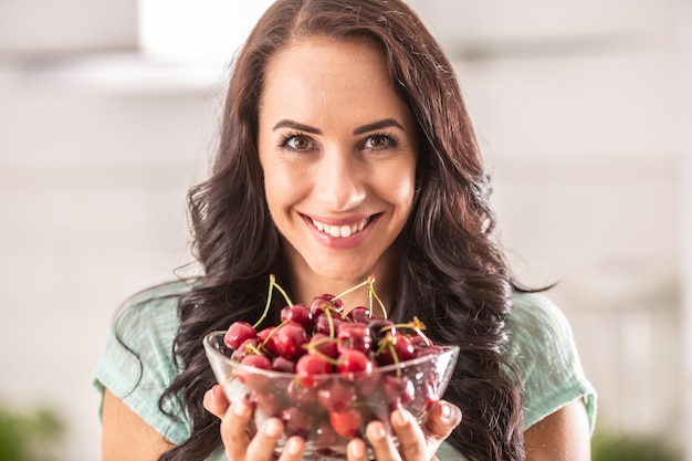 Beautiful woman holding glass bowl full of fres cherries.