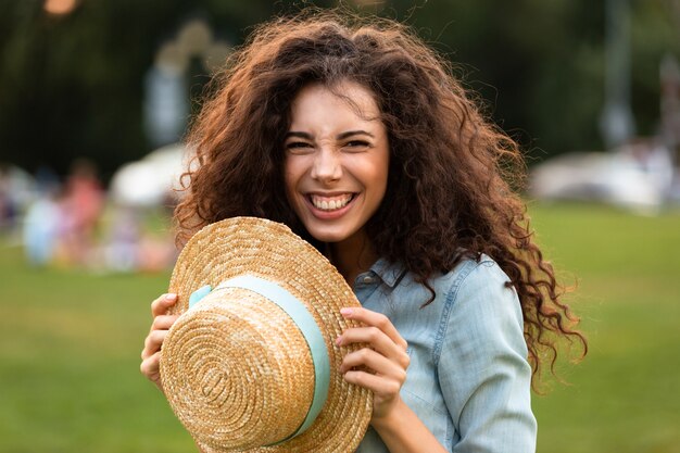 beautiful woman holding straw hat and laughing, while walking in green park