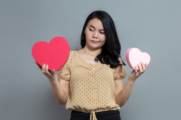 Beautiful woman holding two heart shaped gift boxes with sullen facial expression