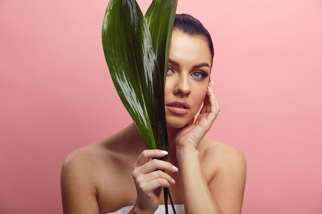 Beautiful woman holds tropical leaf near her face on a pink isolated