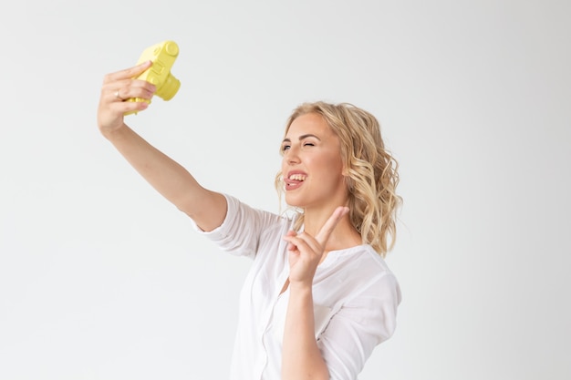 Beautiful woman holds yellow retro camera on white wal