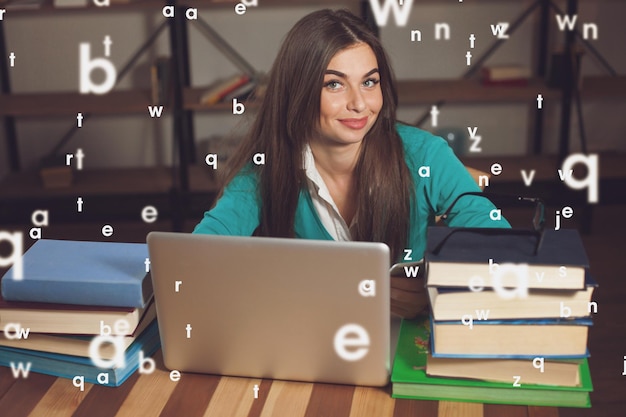 Beautiful woman is happy about her successful work with her grey laptop and books at the wood table