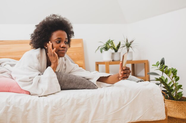 The beautiful woman is lying on the bed in a bathrobe and surfing the internet The woman with smartphone is resting in a hotel