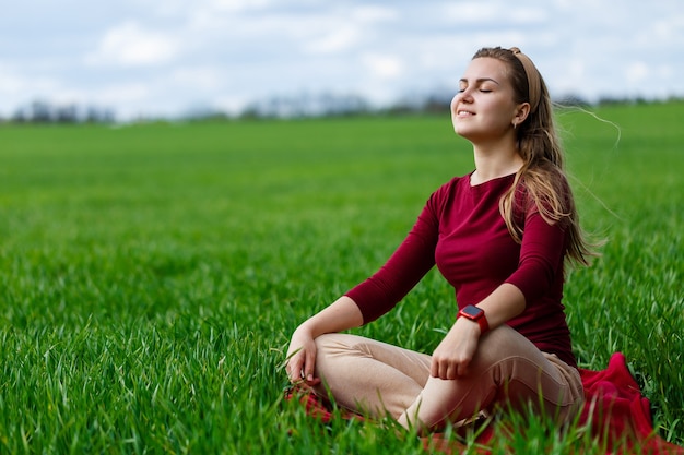 Beautiful woman is sitting on the grass and resting. The girl closed her eyes and enjoyed the sun. She smiles and enjoys a warm day.