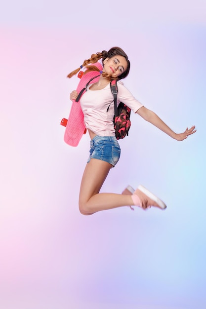 Beautiful woman jumping with longboard on pink background