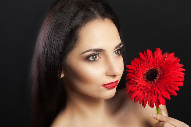 Beautiful woman light makeup on her face in the hands of a beautiful red flowe