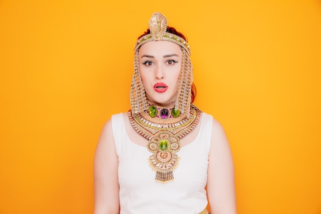 Beautiful woman like cleopatra in ancient egyptian costume confused and surprised on orange