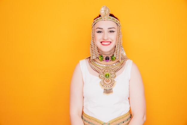 Beautiful woman like cleopatra in ancient egyptian costume happy and positive smiling cheerfully on orange