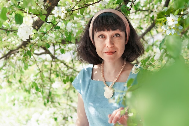 Beautiful woman in a long blue dress with blooming apple trees in the spring garden