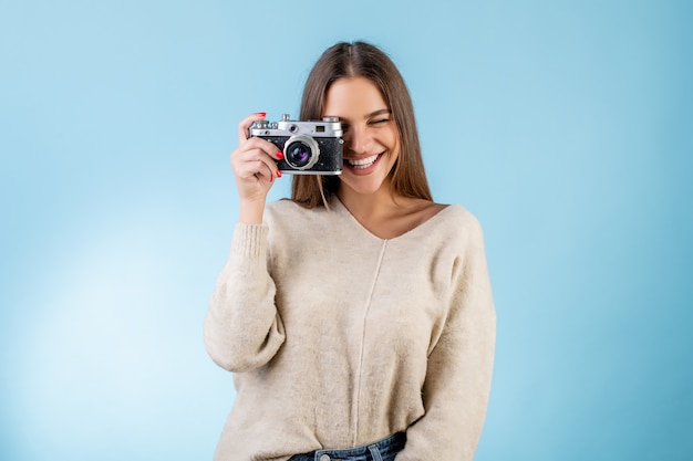 Beautiful woman making picture with vintage photo camera isolated over blue