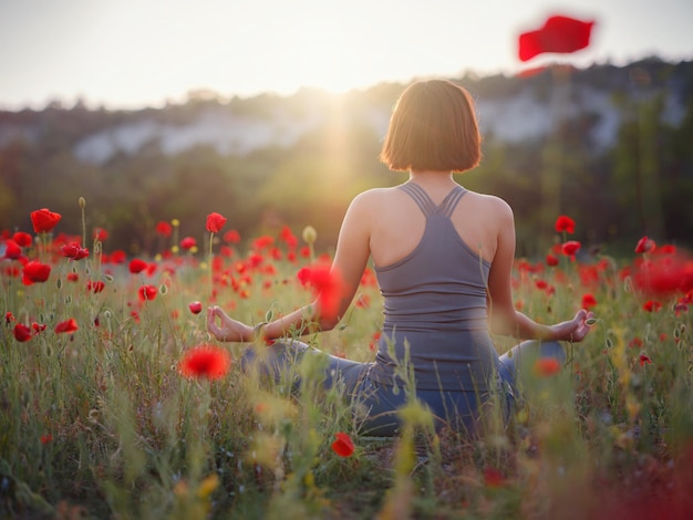 A beautiful woman meditates on a poppy field at sunset