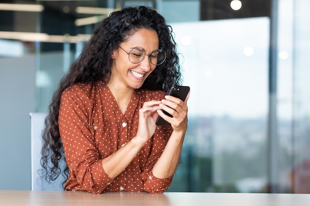 Beautiful woman in the office happy and smiling latin american business woman uses internet phone