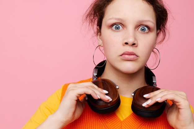 Beautiful woman in an orange sweater headphones music entertainment pink background unaltered