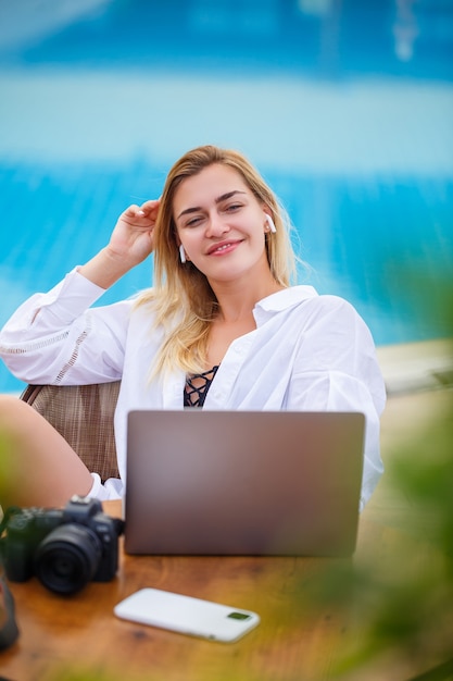 Beautiful woman photographer blogger on vacation, working with laptop by the pool. Freelance remote work