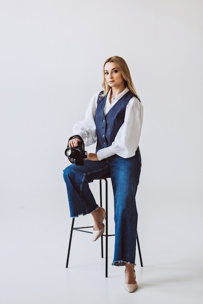 A beautiful woman photographer in a denim casual outfit and a white blouse with voluminous sleeves with a camera in her hands. Hobbies. Soft selective focus.