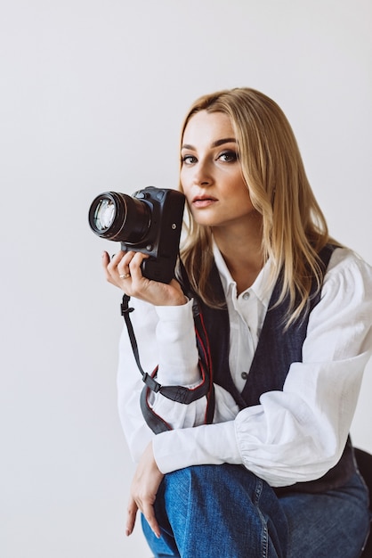 A beautiful woman photographer in a denim casual outfit and a white blouse with voluminous sleeves with a camera in her hands. Hobbies. Soft selective focus.