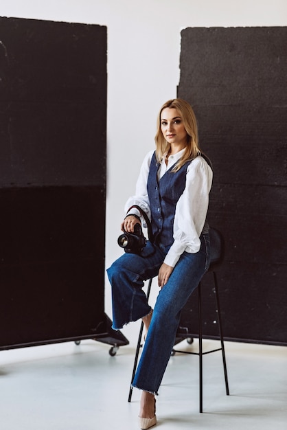 A beautiful woman photographer in a denim casual outfit and a white blouse with voluminous sleeves with a camera in her hands. Hobbies. Soft selective focus.