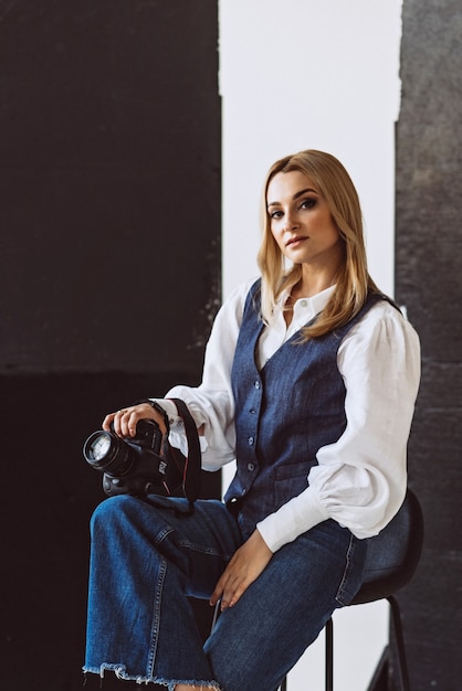 A beautiful woman photographer in a denim casual outfit and a white blouse with voluminous sleeves with a camera in her hands. Hobbies. Soft selective focus.