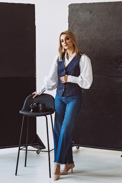 A beautiful woman photographer in a denim casual outfit and a white blouse with voluminous sleeves with a camera in her hands. Hobbies. Soft selective focus.