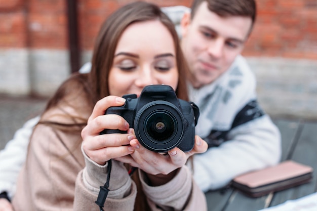 Beautiful woman photographer makes photos outdoor in winter together with her smiling happy boyfriend