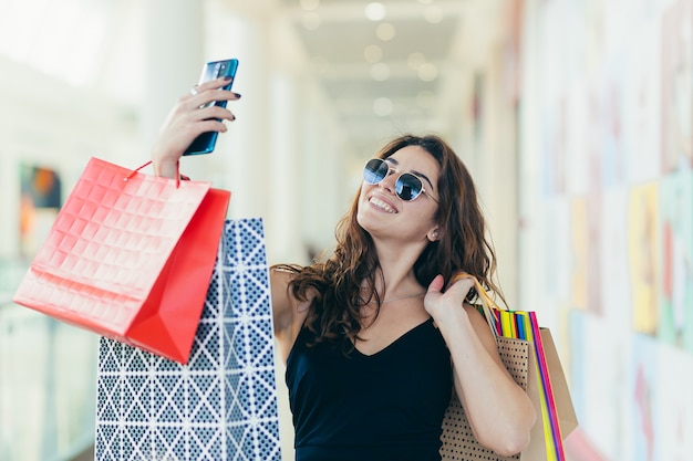 beautiful woman, and photographs herself, rejoices in the purchased goods, with colored bags