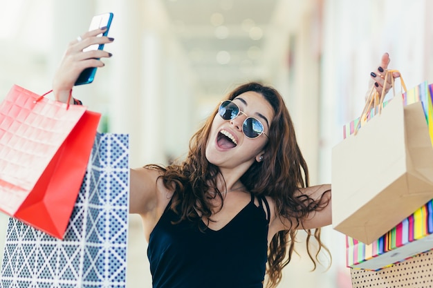 beautiful woman, and photographs herself, rejoices in the purchased goods, with colored bags