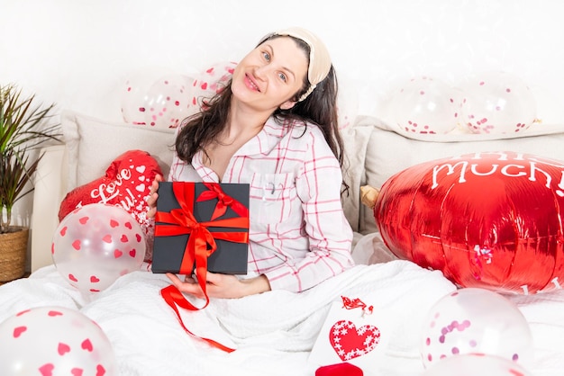 A beautiful woman in pink pajamas with a heartshaped balloon lies on bed at home