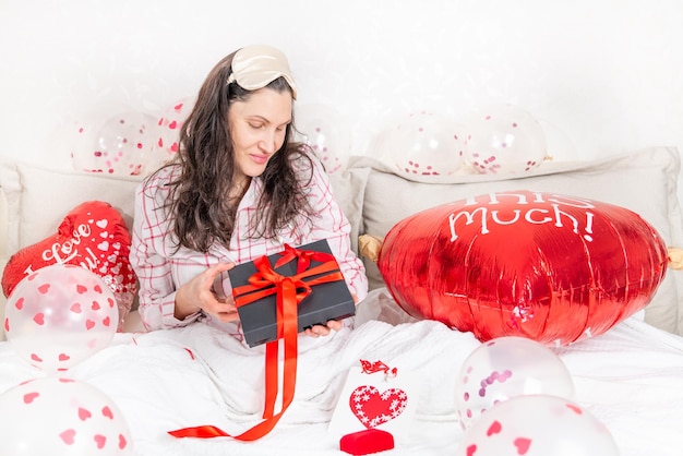 A beautiful woman in pink pajamas with a Valentines heart-shaped balloon lies on bed at home