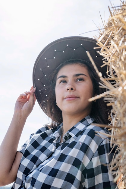 Beautiful woman in plaid shirt and cowboy hat resting on haystack