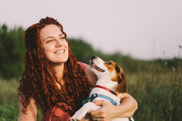 Beautiful woman plays with her Jack Russell dog in the park The concept of animals friendship people and love a woman lies on the grass and plays with a jack russell terrier