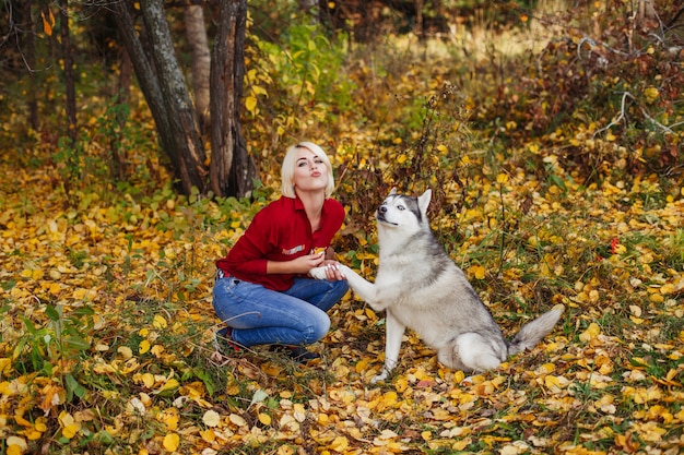 Beautiful woman plays with husky dog in autumn forest