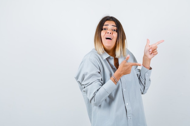 Beautiful woman pointing right in shirt and looking bewildered. front view.