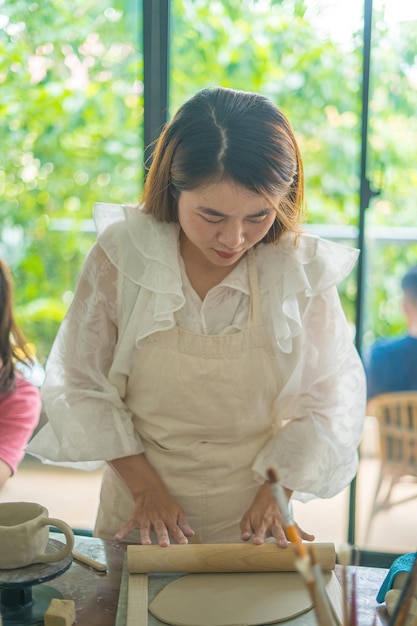 Beautiful woman potter working on potters wheel making ceramic pot from clay in pottery workshop Focus hand young woman attaching clay product part to future ceramic product Pottery workshop