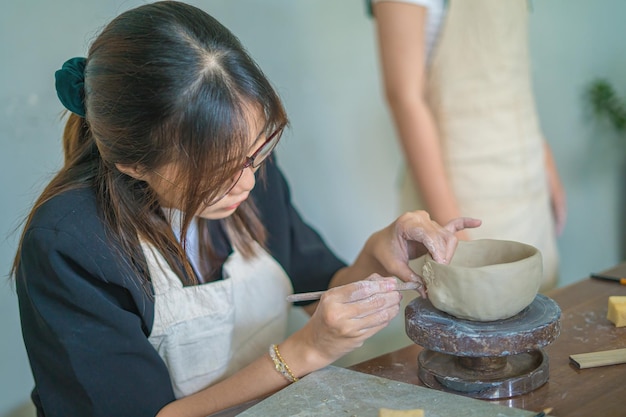 Beautiful woman potter working on potters wheel making ceramic pot from clay in pottery workshop Focus hand young woman attaching clay product part to future ceramic product Pottery workshop