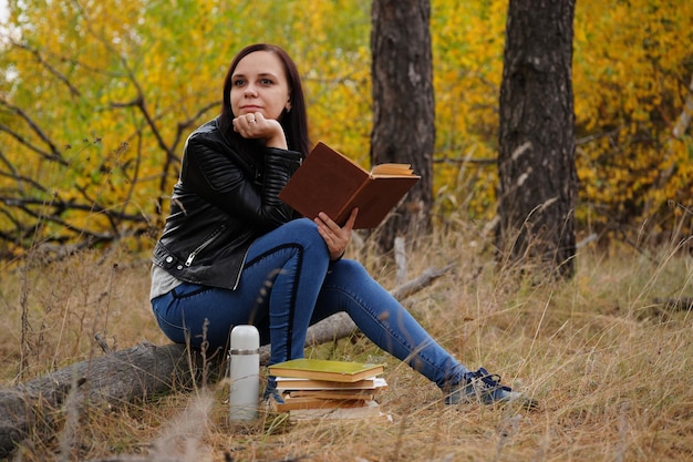 Beautiful woman reading a book in the autumn forest A woman sits near a tree in an autumn forest and holds a book Girl reading a book Autumn season concept and reading